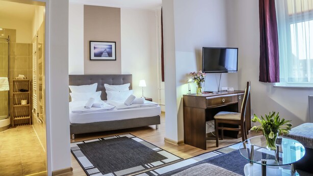 Habitación de hotel con cama, escritorio, silla, televisión y baño con ducha e inodoro.