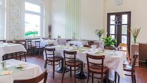 Un restaurante con varias mesas dispuestas para comer, sillas de madera y plantas en macetas.