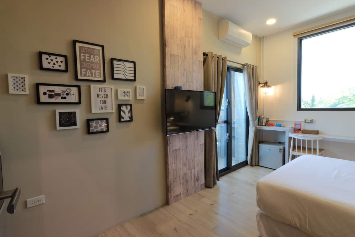 A hotel room with a bed, a TV, a desk with a chair, a small fridge, and a window with curtains.