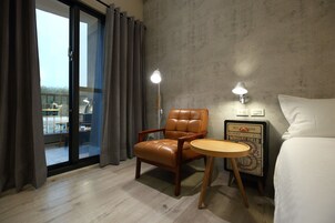 Habitación de hotel con una butaca de cuero, una mesita redonda pequeña, una cama y vistas a través de una puerta corredera.
