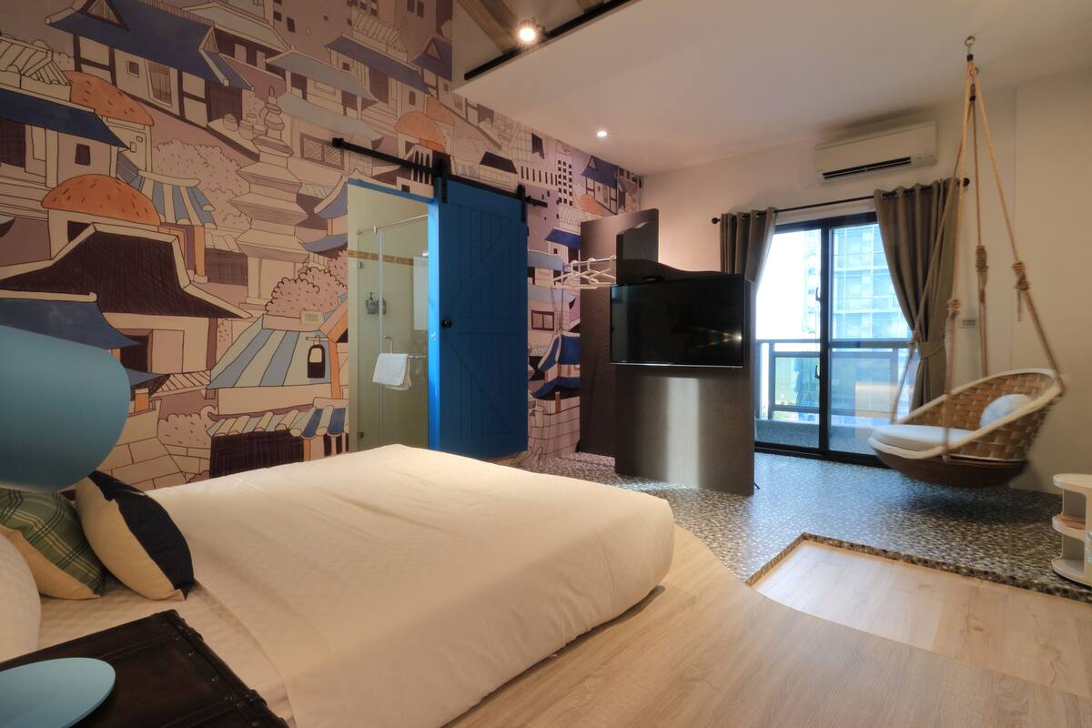A bedroom with a bed, a television, a hanging chair, and a cityscape mural on the wall.