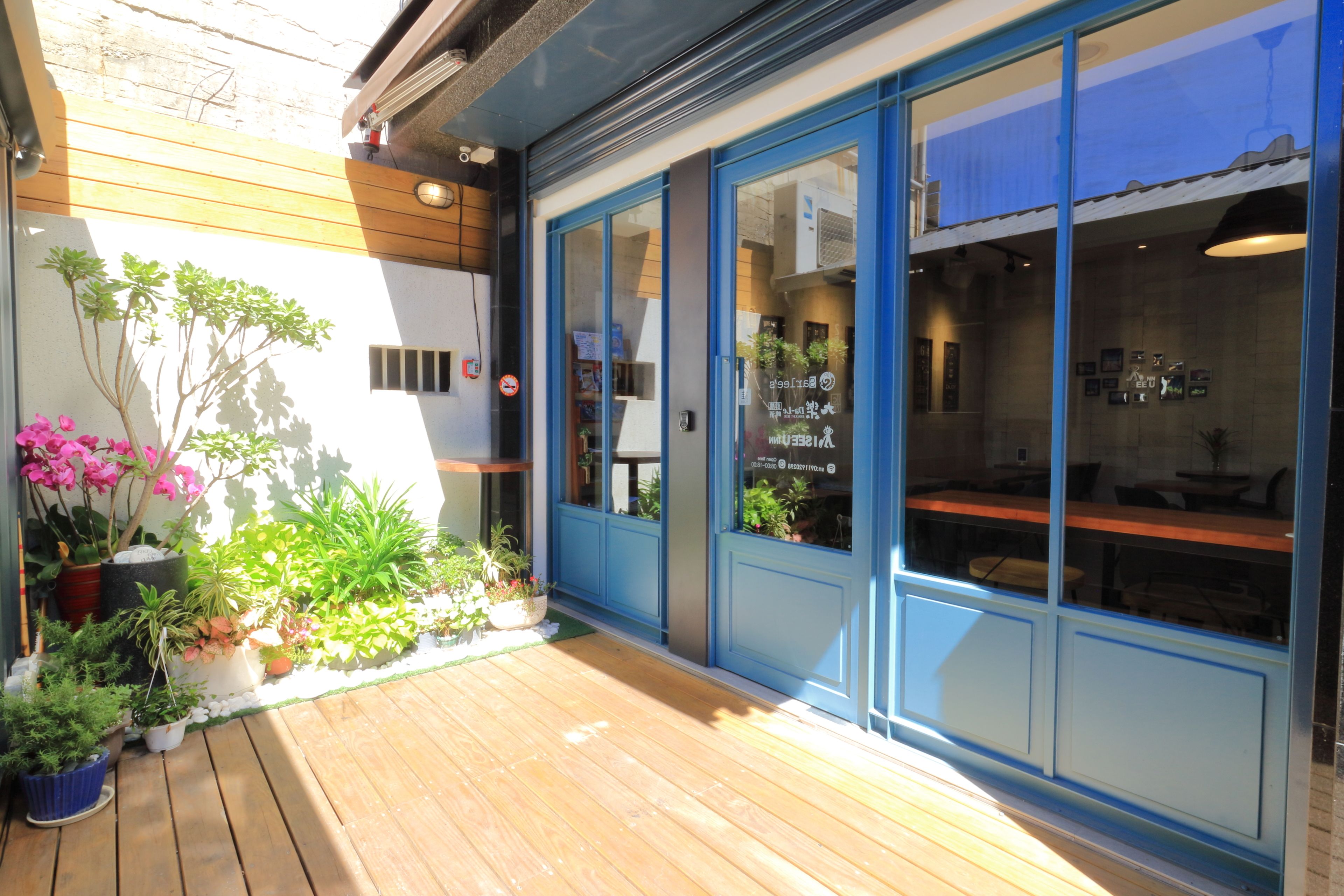 A wooden deck with potted plants and a blue-framed building with glass doors.