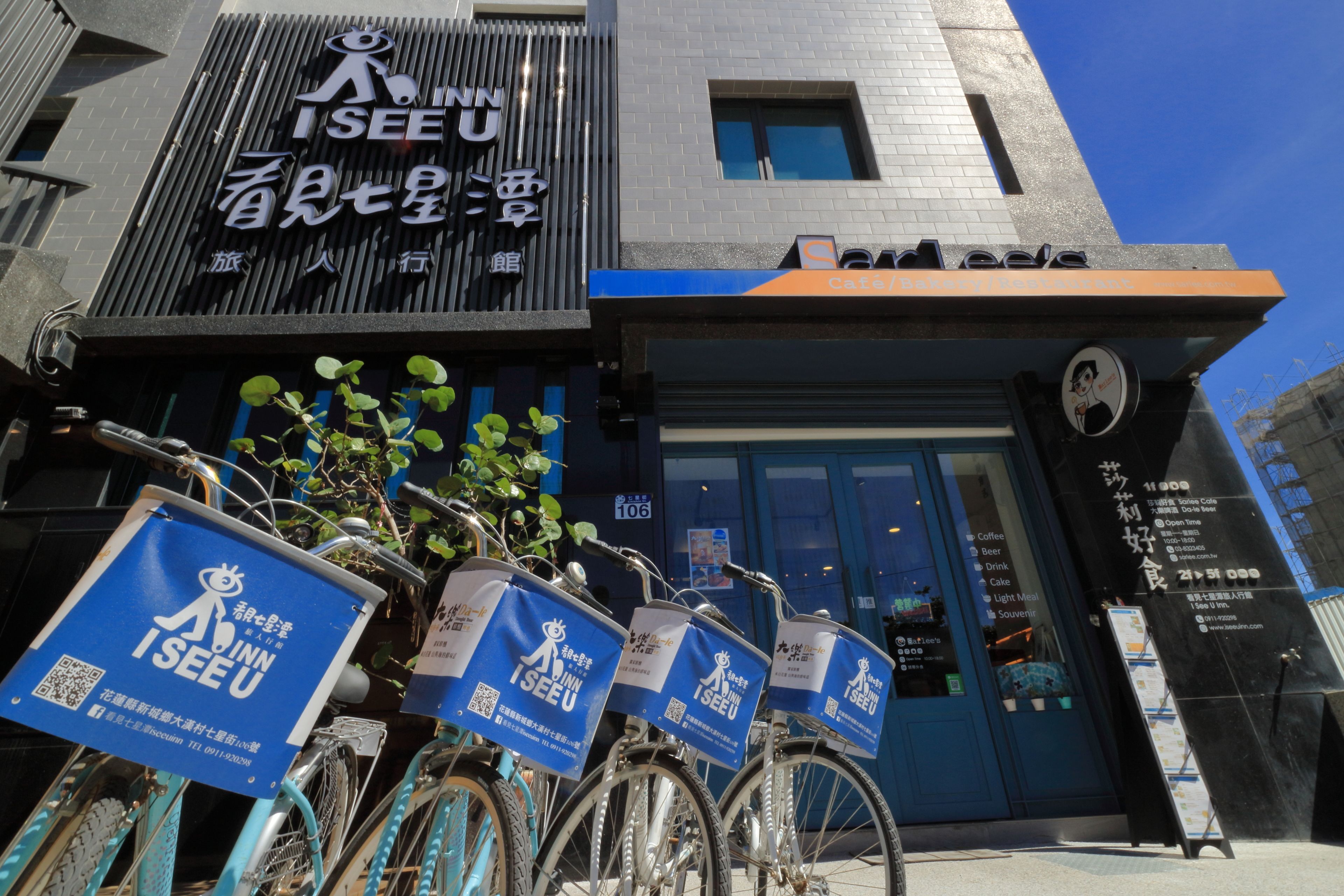 A building with a sign reading "I SEE U" and a blue storefront. There are three bicycles with blue signs in front of the building.