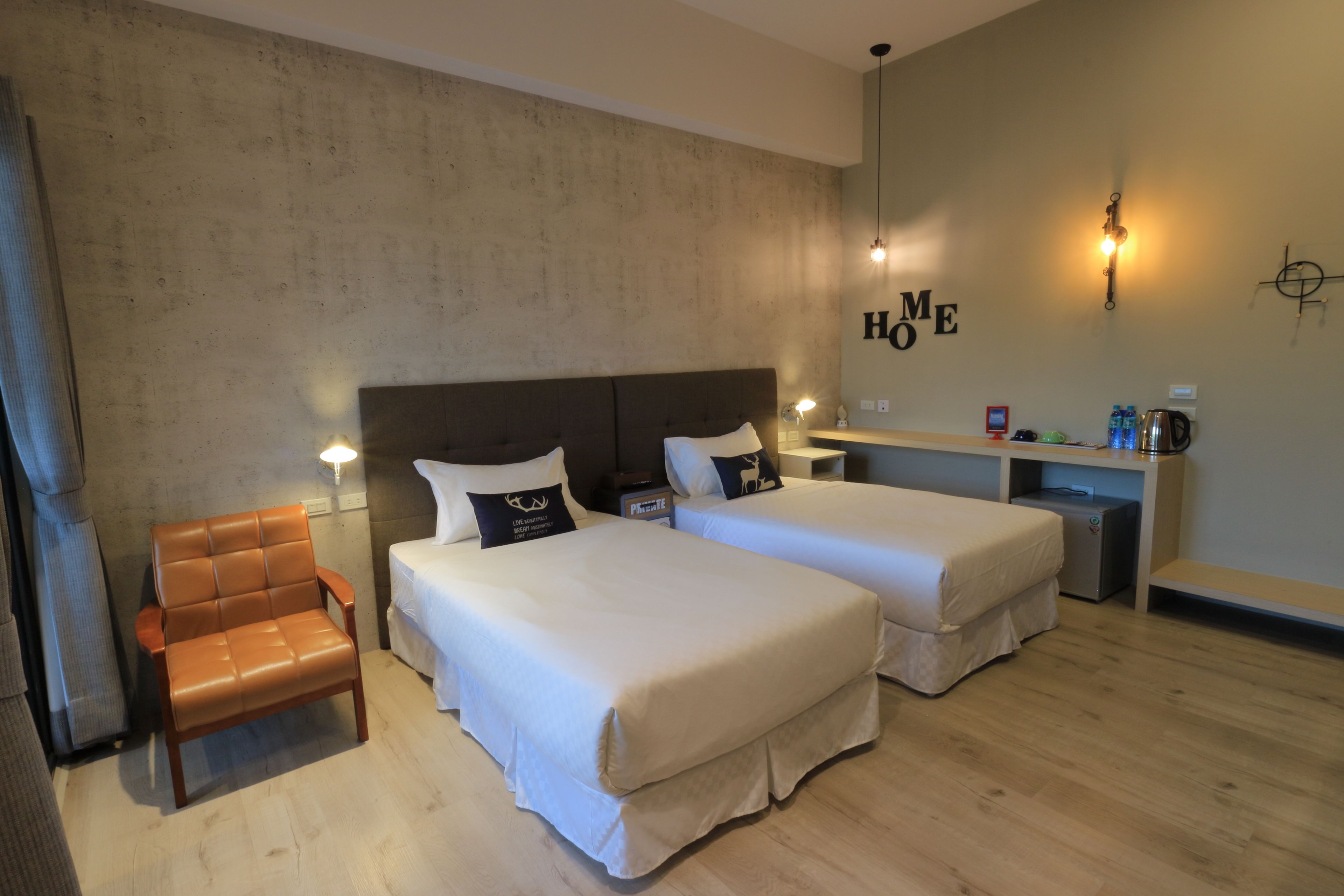 A hotel room with two beds, a wooden chair, a nightstand, and a shelf with toiletries.