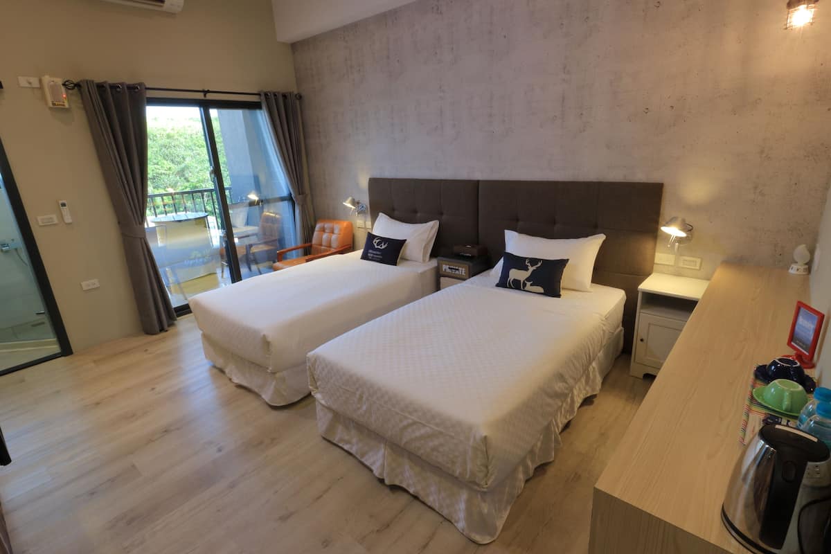 A hotel room with two beds, a wooden desk, a nightstand, and a view of the outdoors.