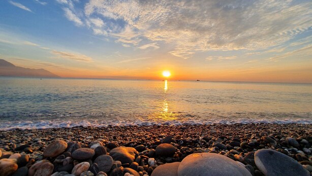A beach with pebbles and a sunset over the water. - I See U Inn (Xincheng)