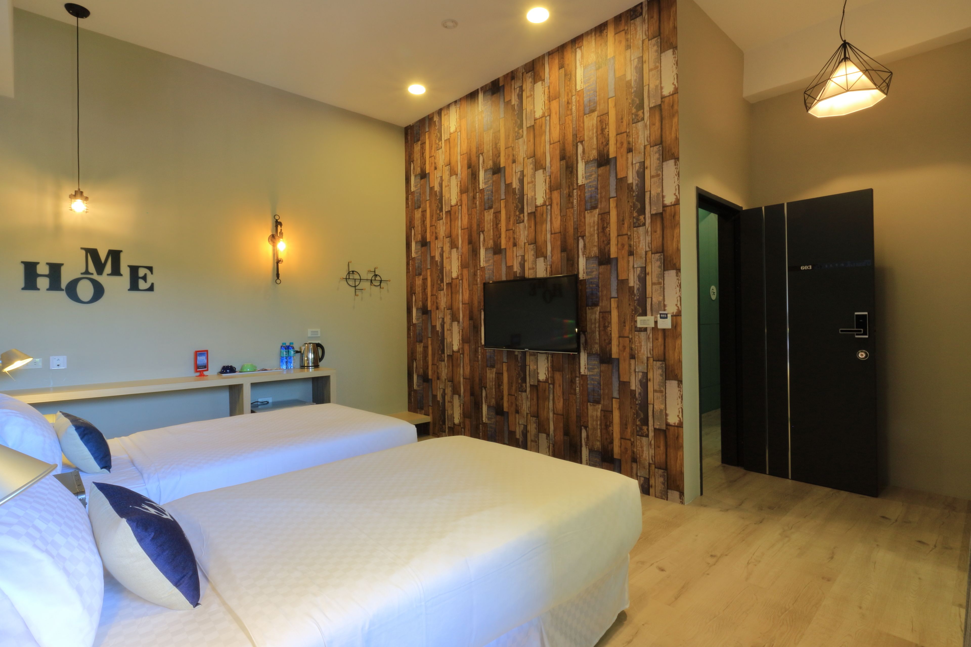 Ein Hotelzimmer mit zwei Betten, einer Wand mit Holzverkleidung, einem Flachbildfernseher, einer Minibar und einer verschließbaren Tür.