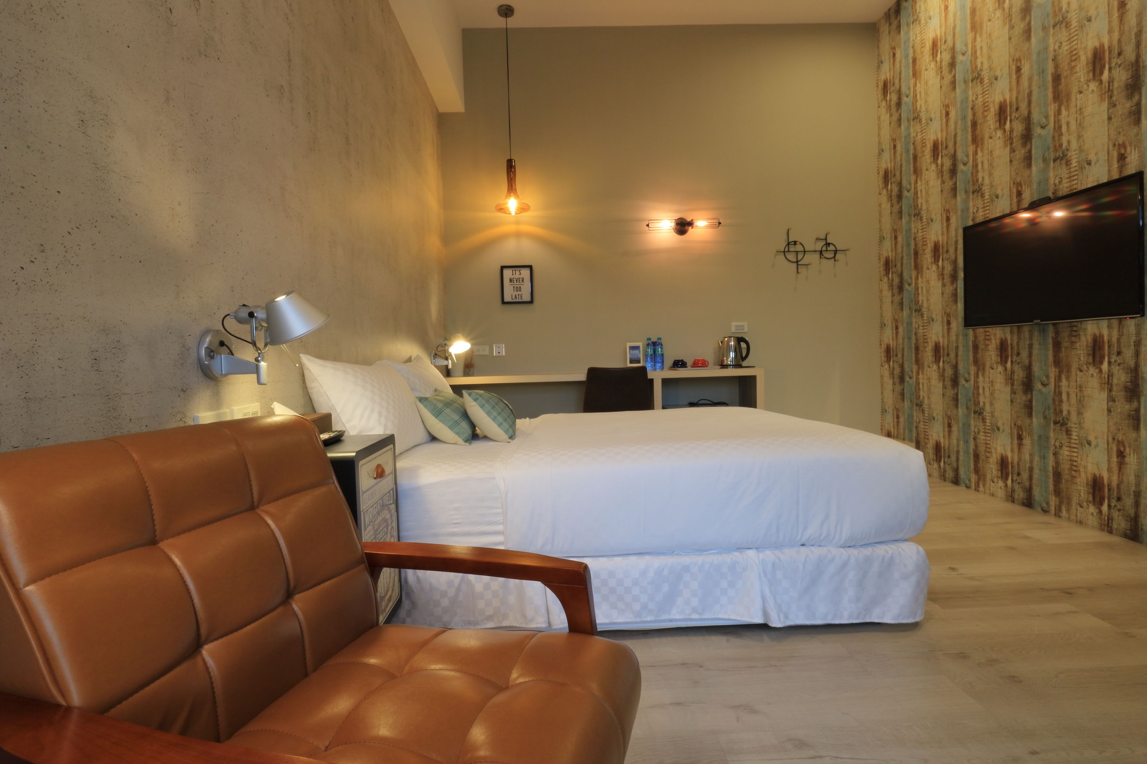 A bedroom with a bed, a chair, a nightstand, a lamp, a TV, and a wall with a wooden panel design.