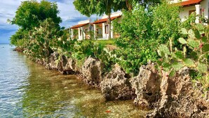 Un hotel frente al mar con aguas cristalinas, costa rocosa y abundante vegetación.