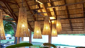 Un restaurante con techo de paja, lámparas de mimbre colgantes y grandes plantas verdes.