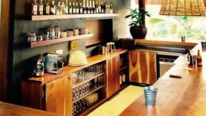 Un área de bar con techo de madera, una lámpara colgante, estantes con botellas y una barra con vasos.