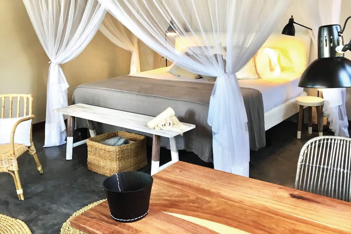 A bedroom with a bed, bedside table, lamp, and a chair.