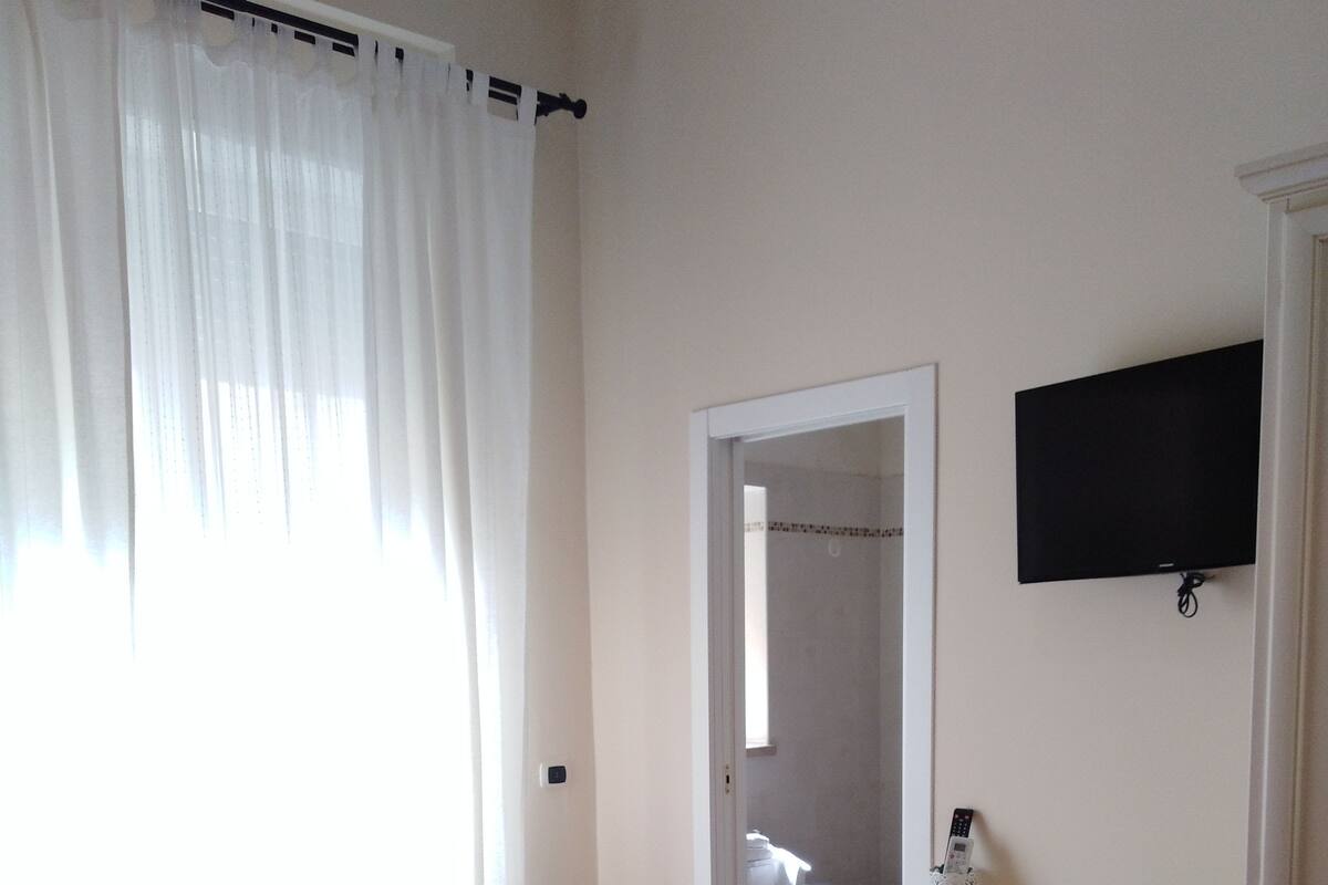 Habitación de hotel con dos camas rojas, un escritorio, una silla, un televisor y un baño visible a través de una puerta abierta.