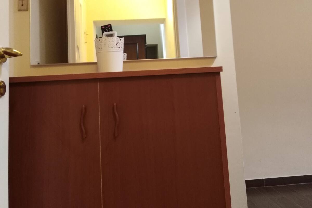 Un armario de madera con un espejo que refleja una habitación con una puerta y un interruptor de luz.