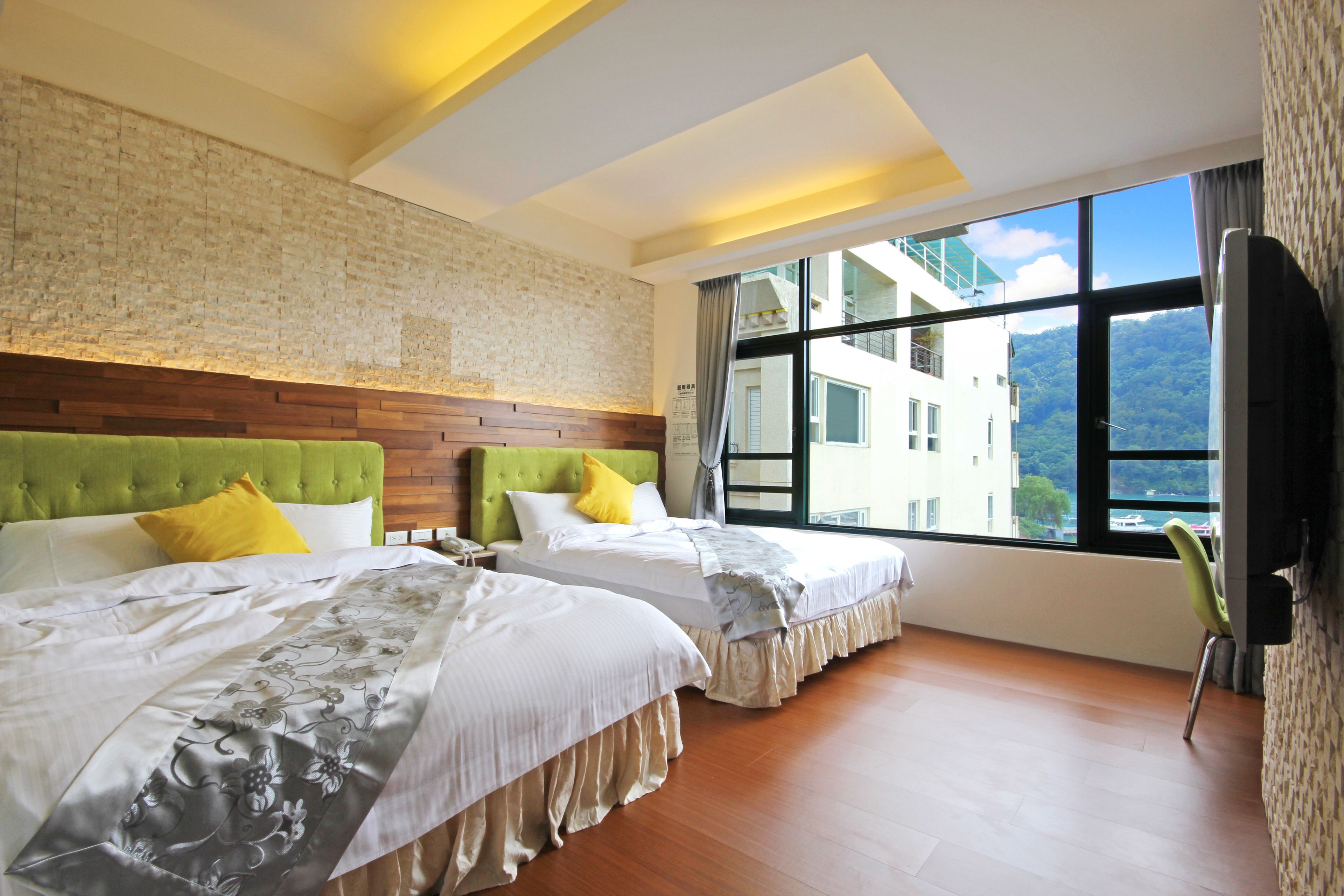 Habitación de hotel con dos camas, una pared de ladrillo, un ventanal con vistas y una silla verde.