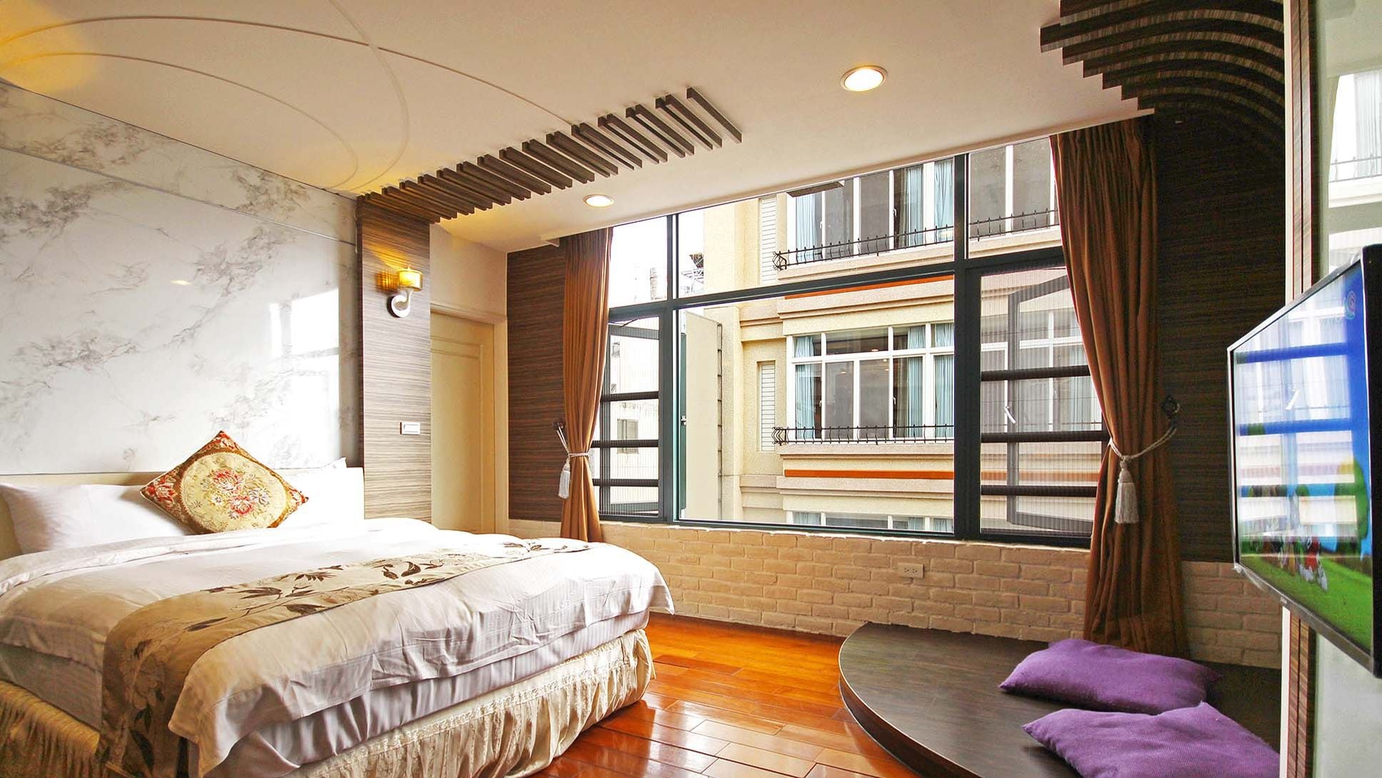 A modern bedroom with a large bed, a TV, and a view of a building through a large window.