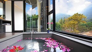 A modern bathroom with a glass shower, a large window with a mountain view, and rose petals on the floor. - Shuian Lakeside Hotel (Yuchi)