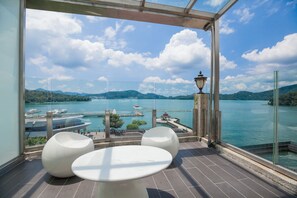 A balcony with a glass railing, offering a view of a lake with boats, a gazebo, and mountains in the background. - Shuian Lakeside Hotel (Yuchi)