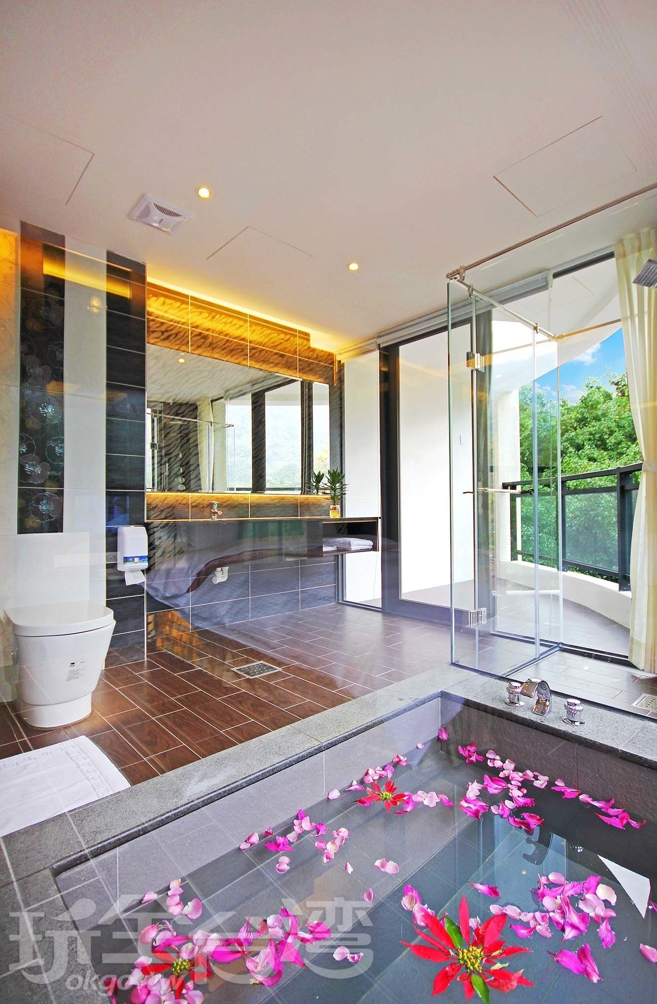 A modern bathroom with a glass shower enclosure, a marble-tiled floor, and a large window offering a view of greenery.