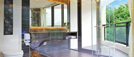 A modern bathroom with a glass shower enclosure, a marble-tiled floor, and a large window offering a view of greenery.