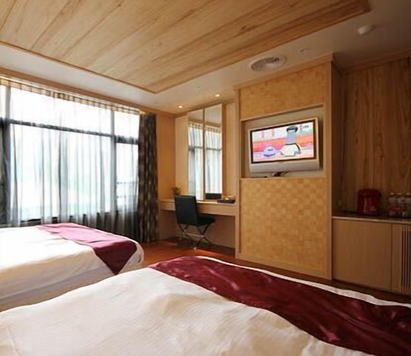Habitación de hotel con dos camas, un escritorio, una silla, un televisor y una ventana con cortinas.