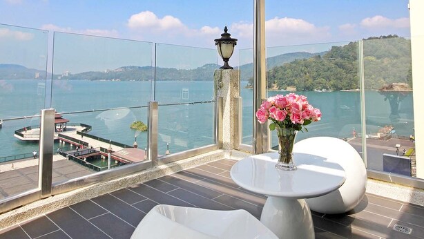 A modern balcony with a glass enclosure, a white table, and a vase of pink flowers. - Shuian Lakeside Hotel (Yuchi)
