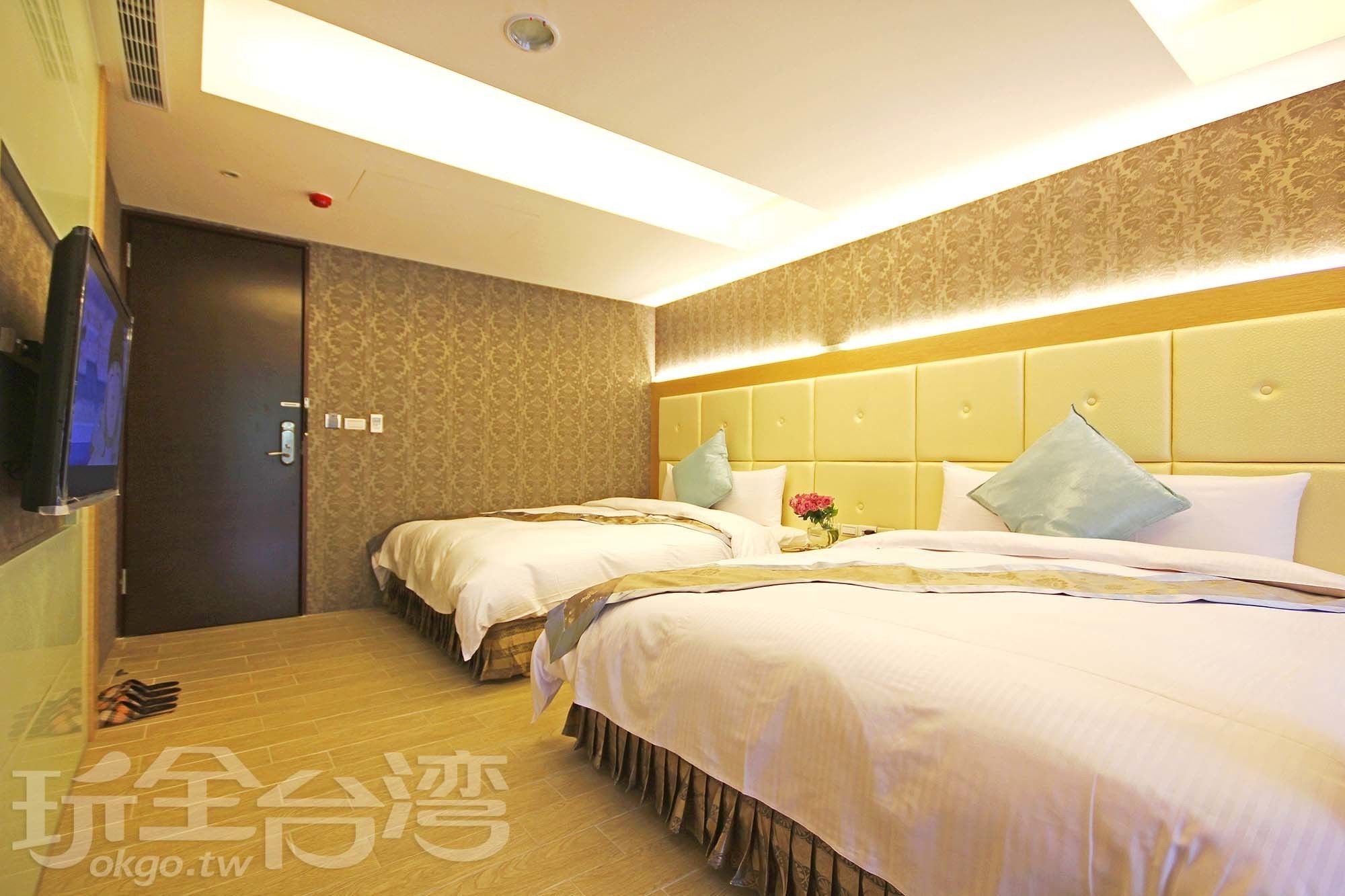 A hotel room with two beds, a television, and a wooden floor.