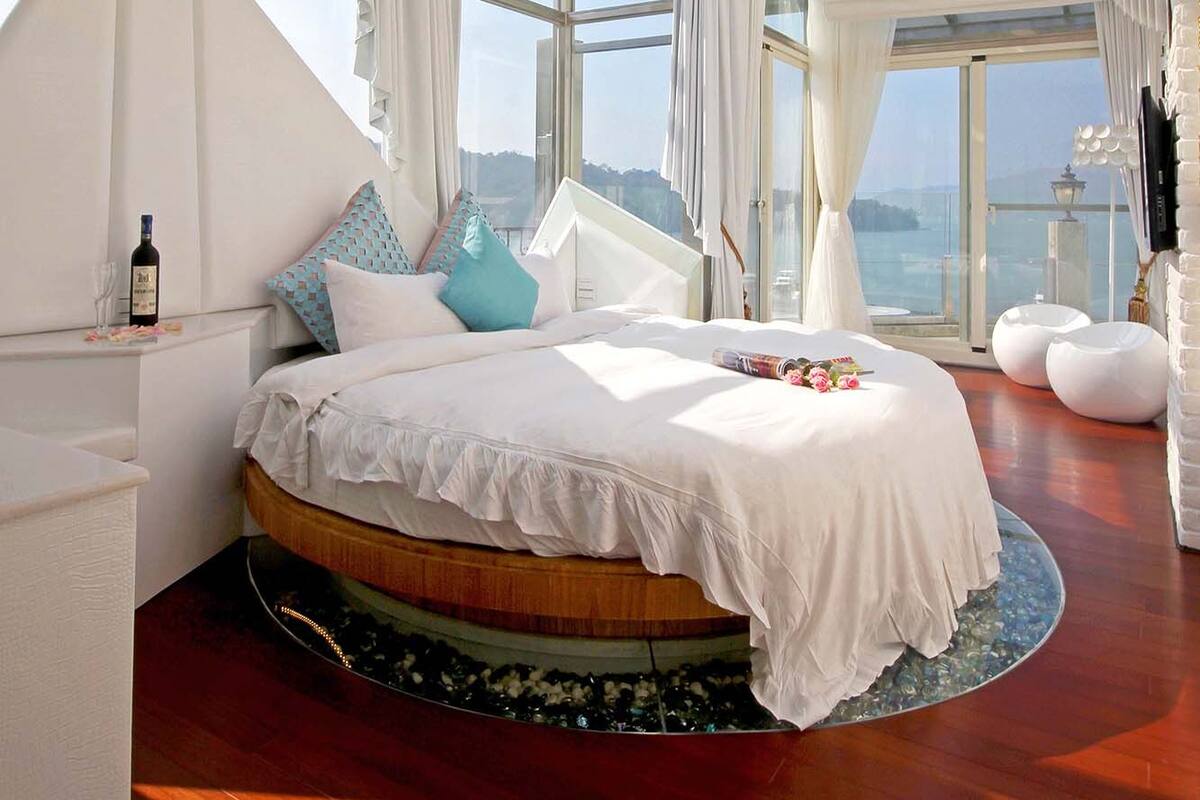 A spacious bedroom with a large bed, a view of the sea, and a glass ceiling.