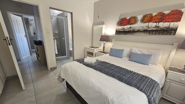 Une chambre à coucher bien rangée, avec un lit, des tables de chevet, une commode, un miroir et un tableau accroché au mur.