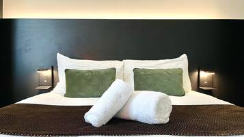 A neatly made bed with two pillows, a rolled white towel, and a dark brown bedspread.