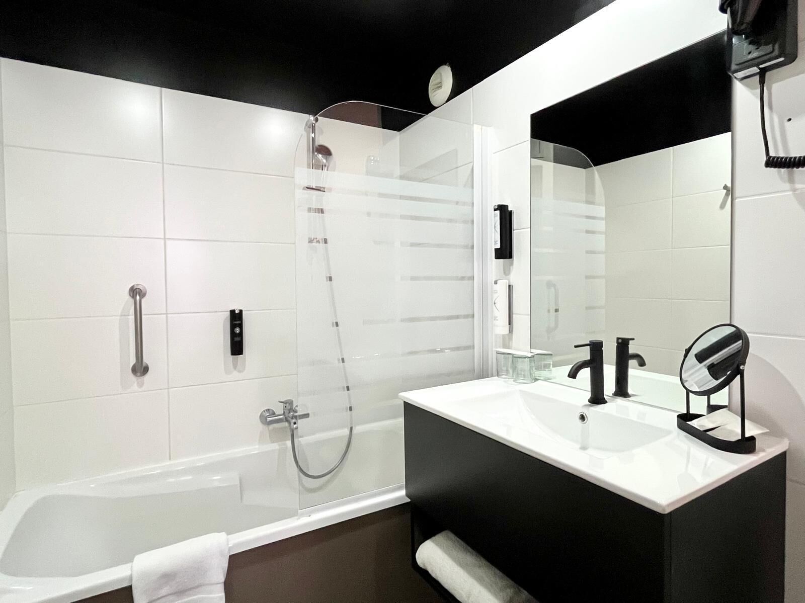 Un baño moderno con ducha de vidrio, un lavabo blanco con grifo negro y un espejo grande.
