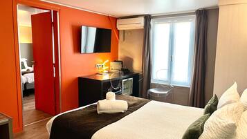 Habitación de hotel con cama, escritorio, televisor y ventana con cortinas.