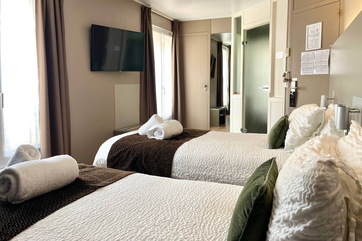 Ein Hotelzimmer mit zwei Betten, einem Flachbildfernseher, einer Tür mit Spiegel und einem Fenster mit Vorhängen.