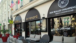 Un hotel con mesas al aire libre y un bar llamado 'Aux Bulles Champagne'.