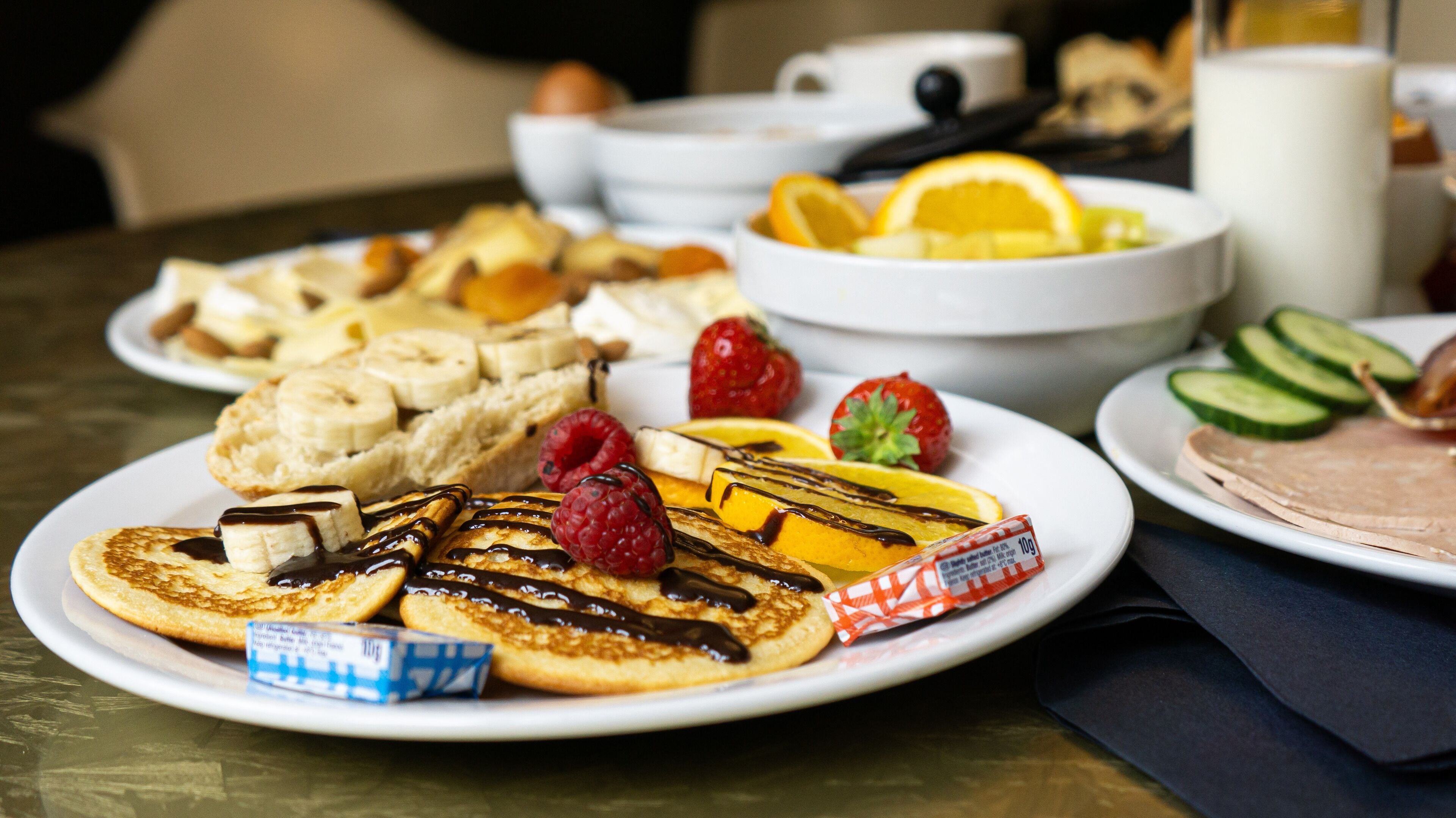 Una mesa con un desayuno que incluye panqueques, frutas y una rebanada de carne.
