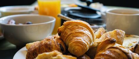 A breakfast setting with croissants, a glass of orange juice, and bowls of food on a table.