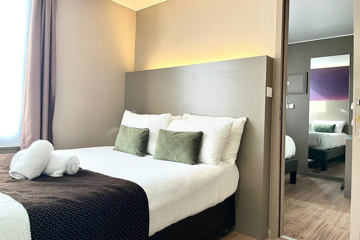 Ein Hotelzimmer mit einem großen Bett, einem Nachttisch, einem Spiegel und Blick auf ein weiteres Zimmer.