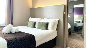 Une chambre d’hôtel avec un grand lit, une table de chevet, un miroir et une vue sur une autre chambre.