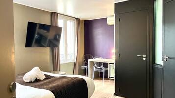 A hotel room with a bed, a desk, a chair, a television, and a door.