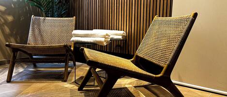 A room with two wicker chairs, a small table with towels, and a wooden slatted wall.
