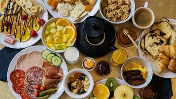 Variedad de alimentos para desayuno, incluyendo bollería, frutas, quesos y embutidos.