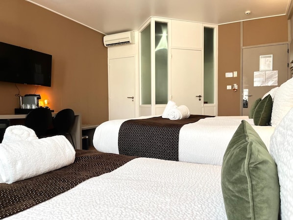 Habitación de hotel con dos camas, un escritorio con computadora, televisor y aire acondicionado.