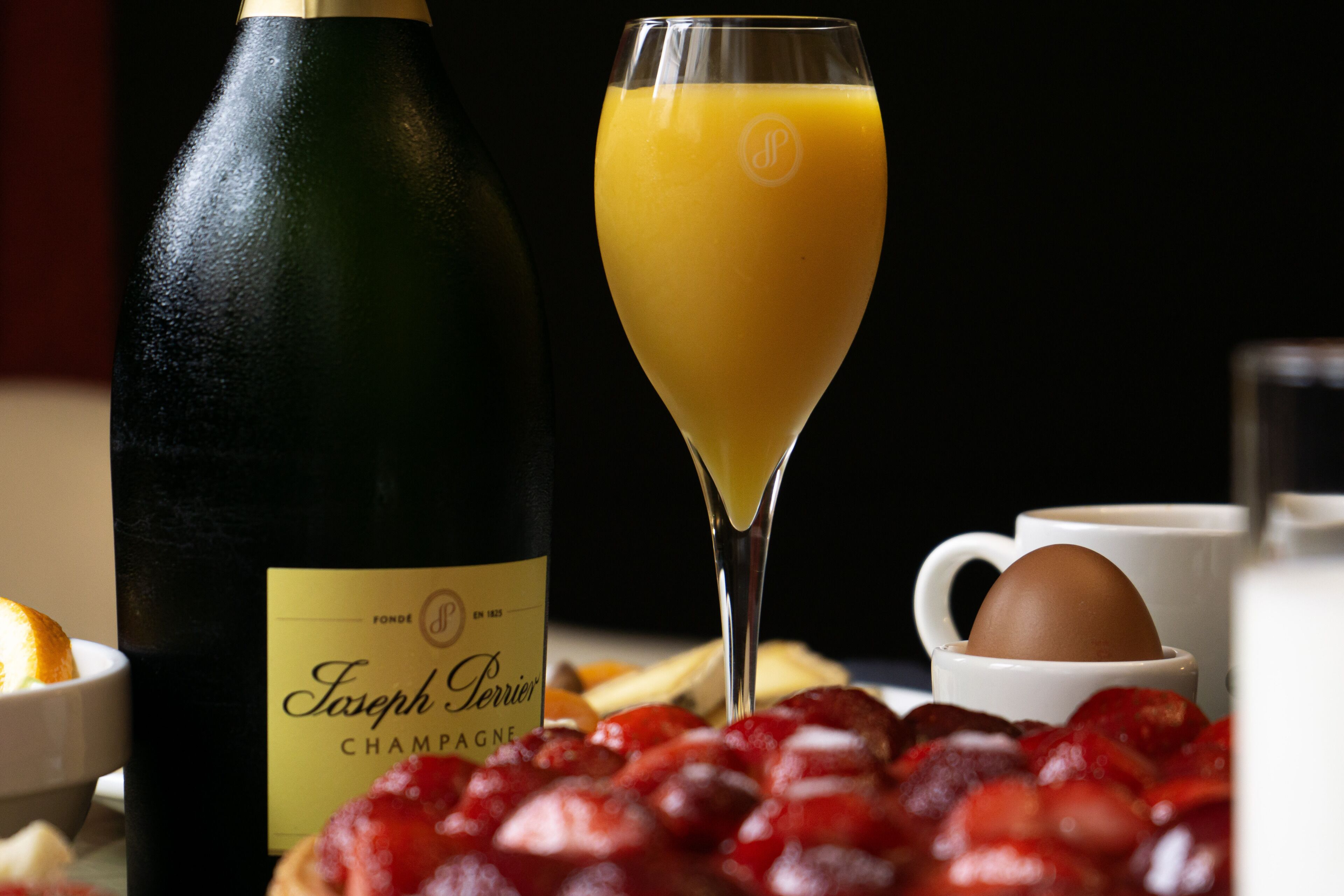 Una botella de champán Joseph Perrier, un vaso de jugo de naranja y un bol de fresas.
