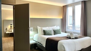 Una habitación de hotel moderna con cama, mesita de noche y vistas al exterior a través de una ventana.