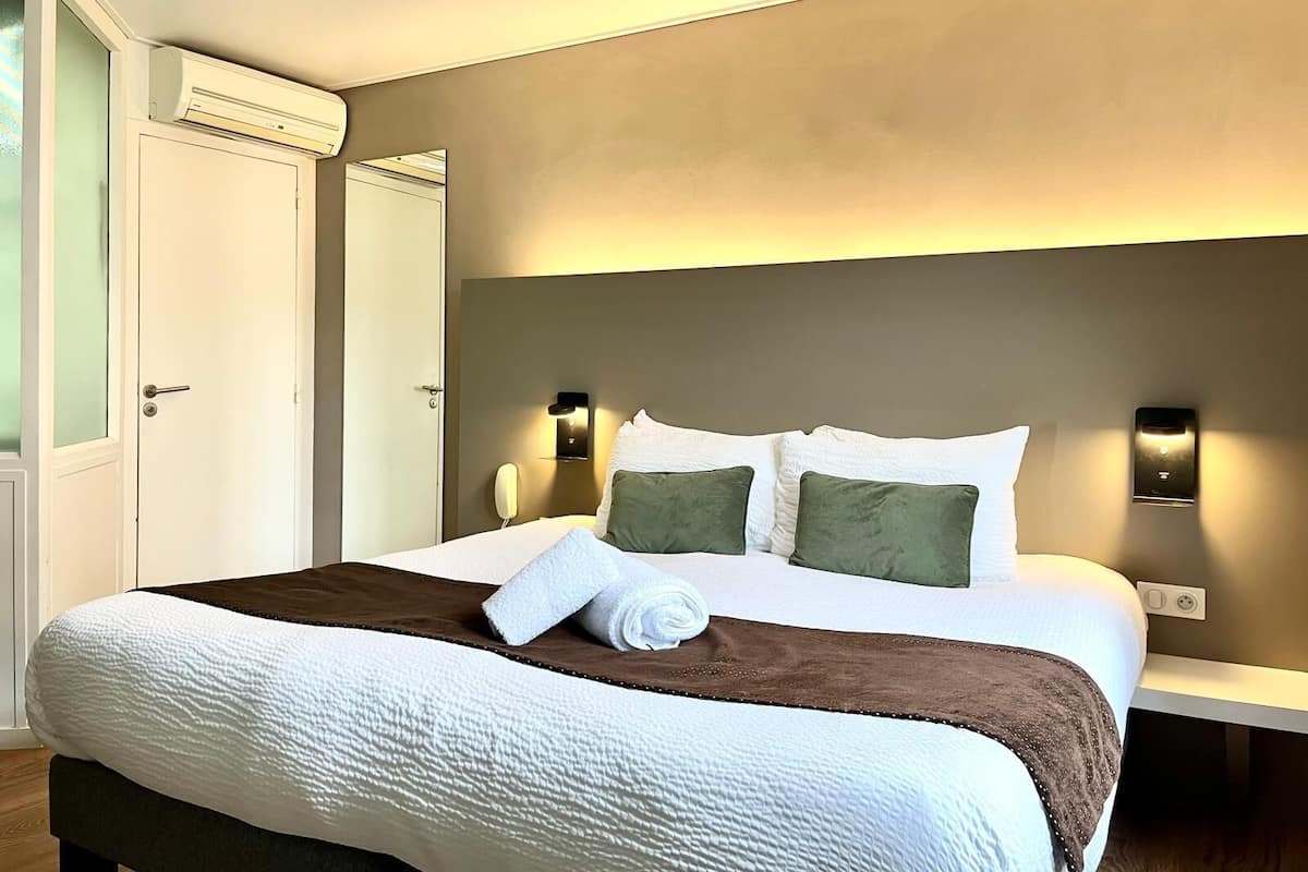 Ein Hotelzimmer mit einem großen Bett, einem Nachttisch, einer Wandleuchte und einer Klimaanlage.