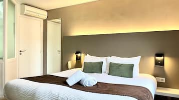 Une chambre d’hôtel avec un grand lit, une table de chevet, une lampe fixée au mur et un appareil de climatisation.