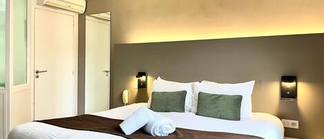 A hotel room with a large bed, a bedside table, a wall-mounted light, and an air conditioning unit.