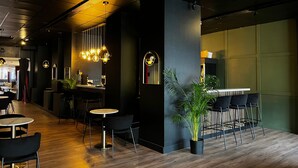 Interior moderno de restaurante con suelo de madera, mesas redondas blancas y negras y lámparas colgantes.