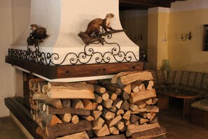 Una chimenea con una repisa decorativa, leña apilada y un sofá al fondo.