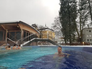 Una piscina con plataforma de madera y un edificio al fondo.